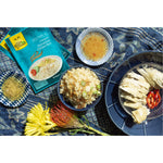 A lifestyle photograph of hainanese rice, steamed chicken, garlic, chili sauces on a picnic blanket is pictured. 
